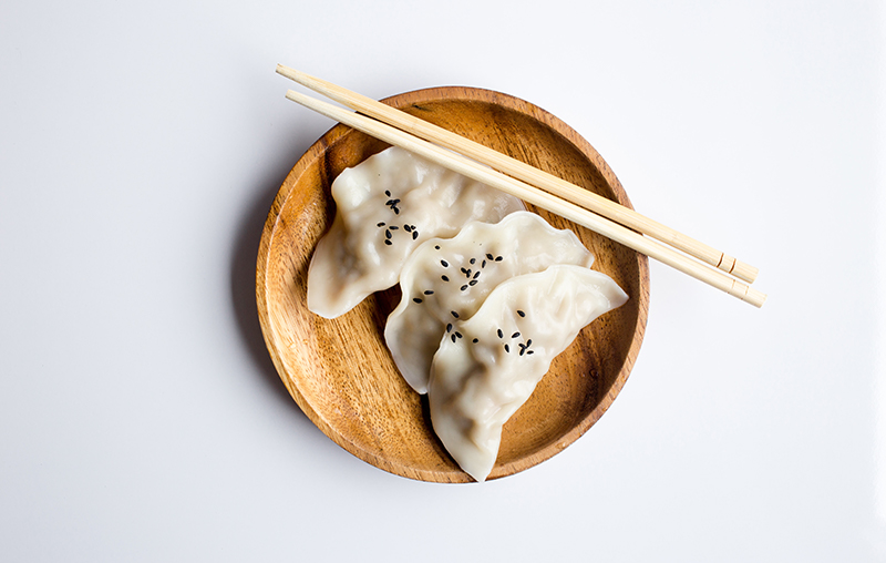 two dumplings on a wood
                            plate with chopsticks